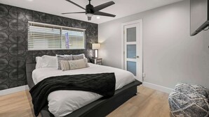 A modern bedroom with a bed, a ceiling fan, a nightstand, and a window with blinds. - Montecito Luxe: 3-Villa Retreat w/ Pool Courtyard (Phoenix)