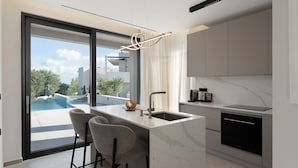 A modern kitchen with a marble countertop, a built-in oven, and a large window overlooking a pool. - Kymothoe Elite Villas (Zakynthos)
