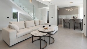 A modern living room with a beige sectional sofa, two round marble tables, and a staircase with glass railings. - Kymothoe Elite Villas (Zakynthos)