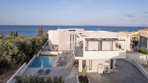A modern building with a pool, outdoor seating, and a view of the sea. - Kymothoe Elite Villas (Zakynthos)