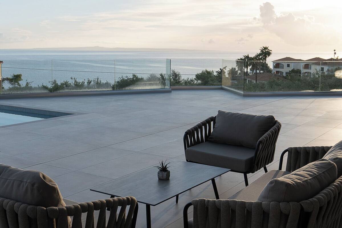 A modern outdoor seating area with a pool, overlooking a coastal landscape.