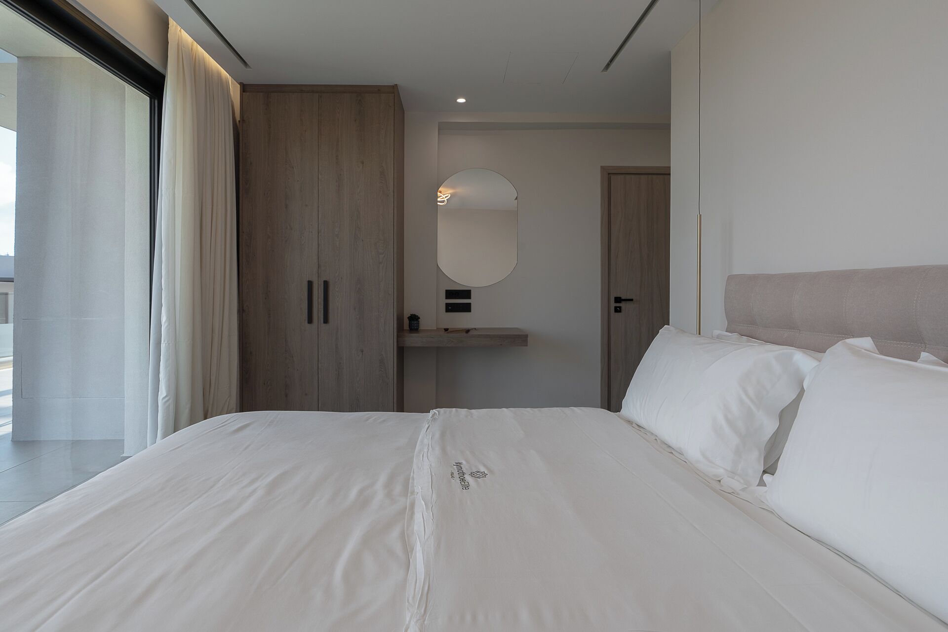 A modern bedroom with a large bed, a wooden wardrobe, a bedside table, and a mirror.