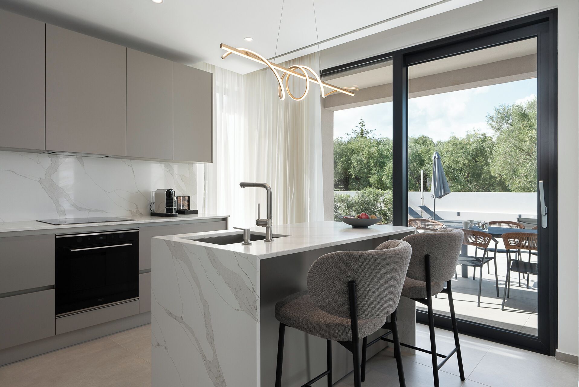 A modern kitchen with a marble countertop, stainless steel appliances, and a large window overlooking a balcony with outdoor seating.