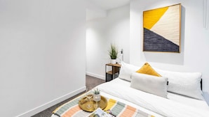 Une chambre d’hôtel moderne avec un lit soigneusement fait, une petite table de chevet agrémentée d’une plante et un grand tableau abstrait accroché au mur.
