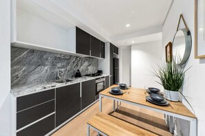 Une cuisine moderne avec des meubles de couleur sombre, un pare-feu en marbre et une table à manger en bois, mise avec des assiettes et un verre.