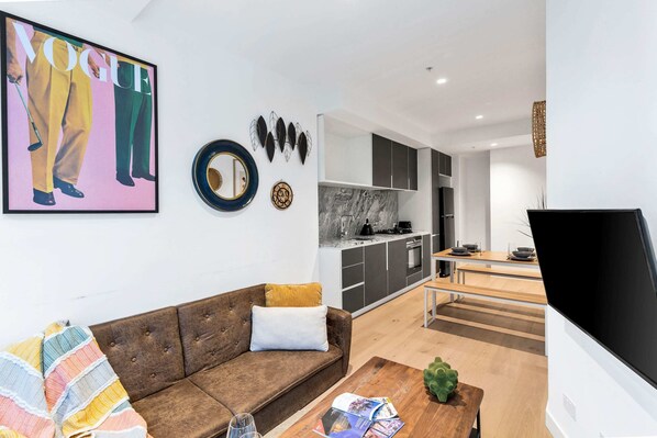 A modern living room with a brown sofa, a coffee table with magazines, and a TV.