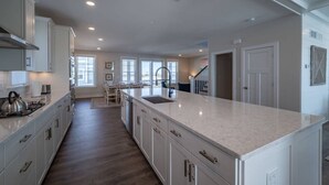 A spacious kitchen with white cabinets, a large island, and a view to the living area. - Coastal Comfort: 4BR 3BH House Pool & Rooftop Deck (Selbyville)