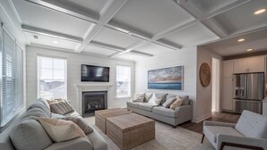 A modern living room with a fireplace, a television, and a kitchen area. - Coastal Comfort: 4BR 3BH House Pool & Rooftop Deck (Selbyville)
