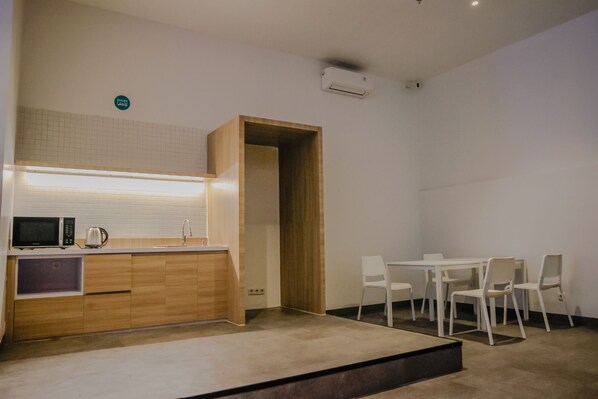 A modern kitchen with a microwave, kettle, and sink. There is a dining area with a table and chairs.