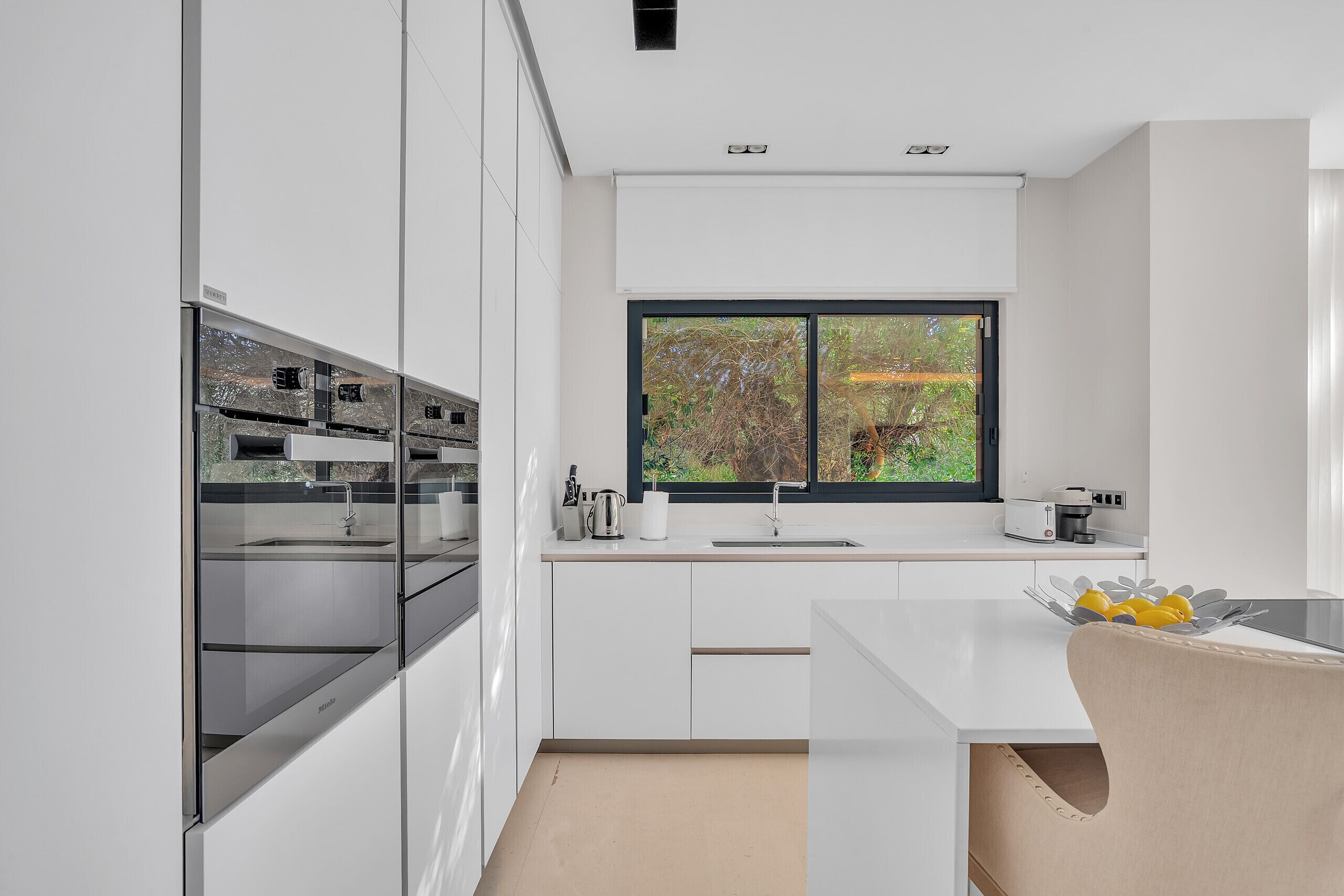 Une cuisine moderne avec des meubles blancs, une grande fenêtre et un four encastré.