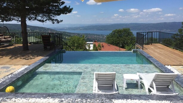 Ein Schwimmbecken mit klarem Wasser, umgeben von einer Holzterrasse und weißen Liegestühlen.