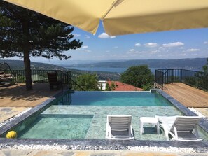 A swimming pool with clear water, surrounded by a wooden deck and white lounge chairs. - Sapanca mavi yeşil köy evi (Sapanca)
