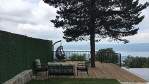 Eine Terrasse mit Hängesessel, Sofa und Blick auf ein Gewässer.