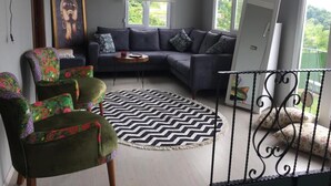 Ein Wohnzimmer mit grauem Sofa, einem gemusterten Sessel, einem schwarz-weißen Teppich und einem Bild an der Wand.