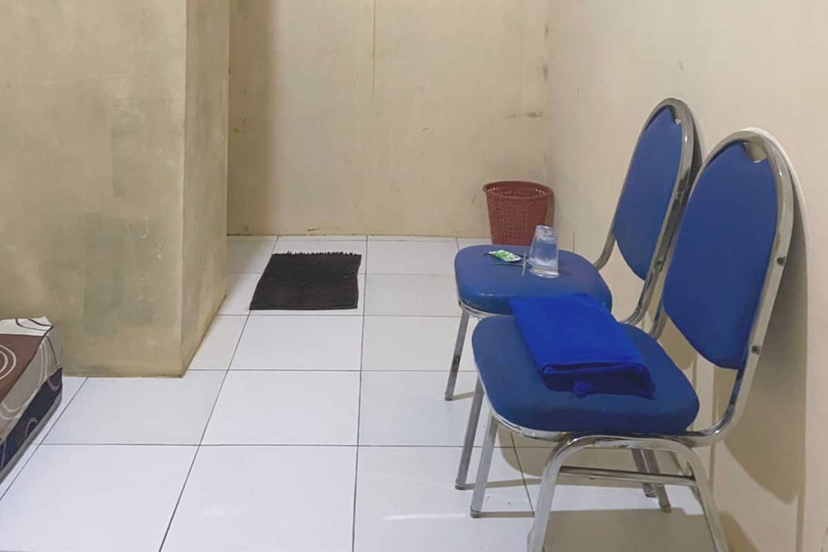 Un espacio pequeño y cerrado con piso de baldosas, dos sillas azules, una cesta roja y una pequeña mesa.