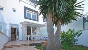 Ein modernes Haus mit Terrasse, Gartenmöbeln und einer Palme.