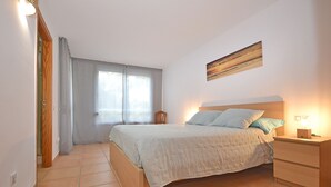 Ein Schlafzimmer mit einem Bett, Nachttischen, einem Sessel, einem Fenster mit Vorhängen und einem Bild an der Wand.