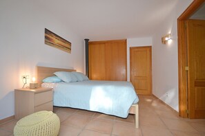 A bedroom with a bed, bedside table, lamp, and a wall-mounted painting.