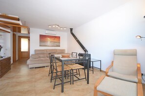 A living room with a sofa, dining table, chairs, a fireplace, and a painting on the wall.