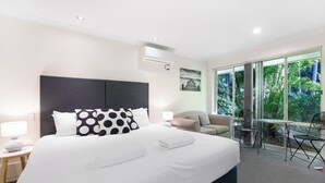 Habitación de hotel con una cama grande, un escritorio, una silla y vistas a zonas verdes a través de amplios ventanales.