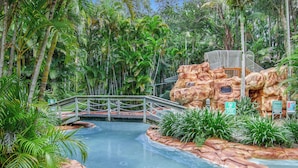 A water slide with a bridge, surrounded by tropical vegetation. - Cuttlefish Cove - 2BR Resort Living by Diggers Beach (Coffs Harbour)
