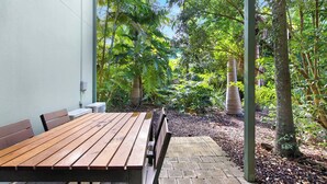 An outdoor patio with a wooden table and benches, surrounded by lush greenery and trees. - Cuttlefish Cove - 2BR Resort Living by Diggers Beach (Coffs Harbour)