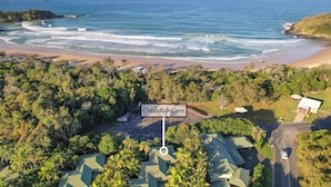 An aerial view of Cuttlefish Cove with a parking area, buildings, and a beach. - Cuttlefish Cove - 2BR Resort Living by Diggers Beach (Coffs Harbour)