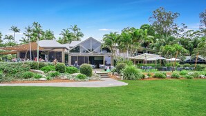 A resort with a large lawn, outdoor seating, and palm trees. - Oceanique - 3BR Tranquil Retreat by Diggers Beach (Coffs Harbour)
