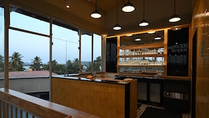 Un espace bar moderne avec un comptoir en bois, de grandes fenêtres et une vue sur les palmiers.