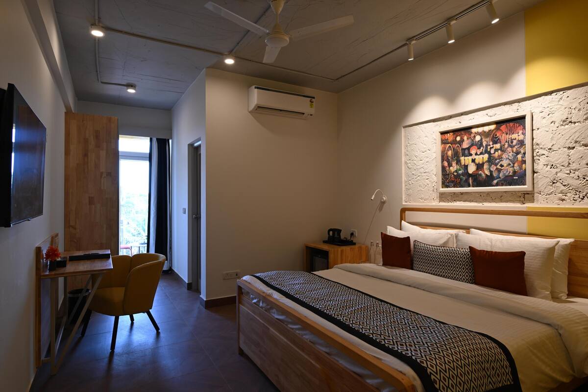 Een moderne hotelkamer met een groot bed, een bureau en een stoel. Er hangt een schilderij aan de muur en er is een airconditioning boven het bed.