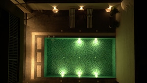Une piscine rectangulaire dont le fond est recouvert de mosaïques vertes, le tout entouré de murs à la finition texturée.