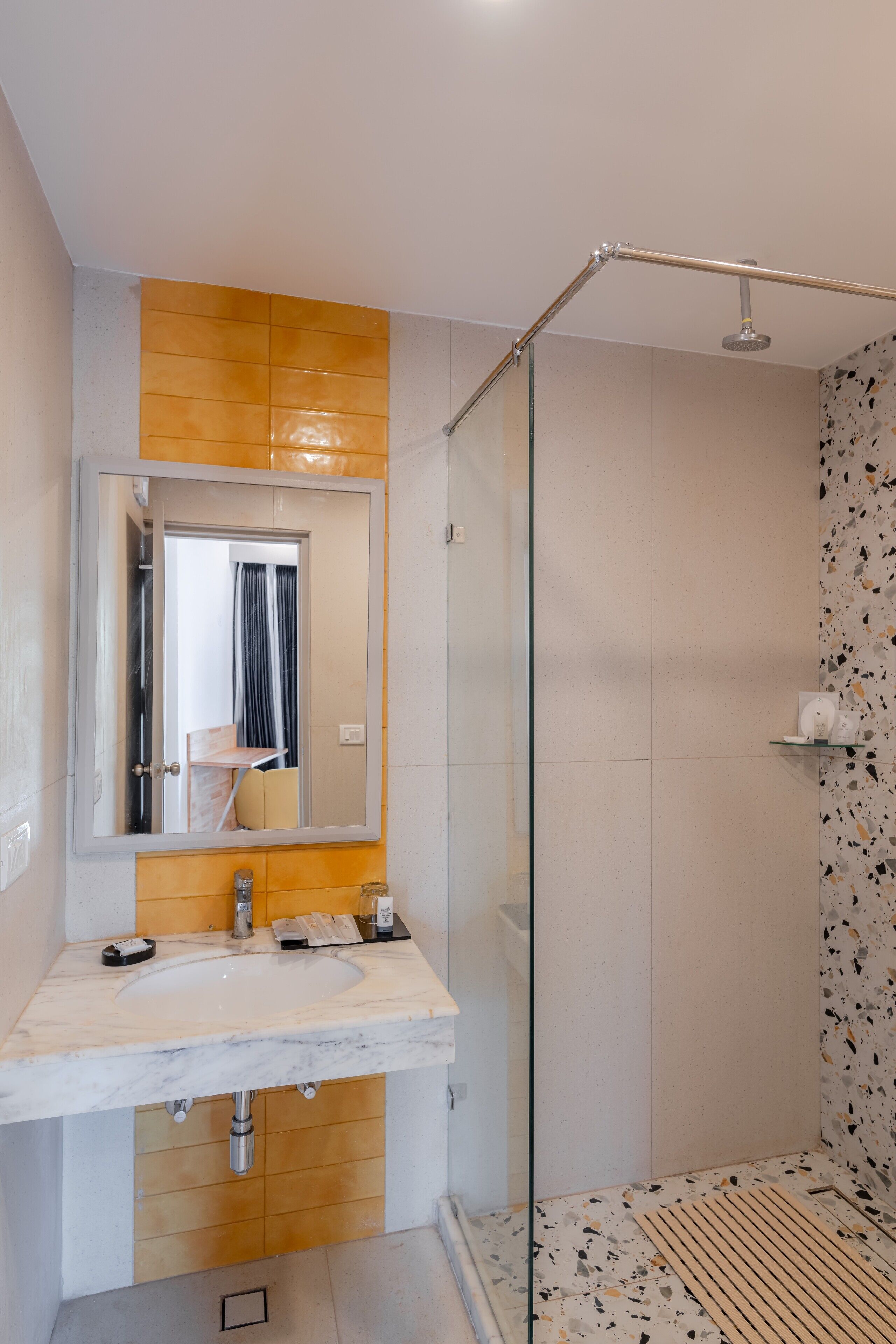 A modern bathroom with a glass shower enclosure, a large mirror, and a marble sink.