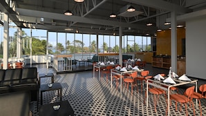 Un restaurant spacieux avec de hauts plafonds, de grandes fenêtres et un sol à motifs. Les tables et les chaises sont disposées de manière ordonnée, et un bar est visible.
