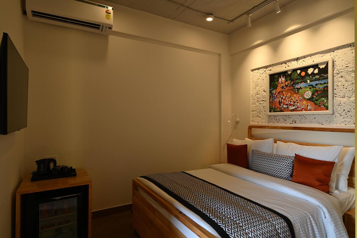Een hotelkamer met een bed, een klein tafeltje met een waterkoker en een wandairconditioner.