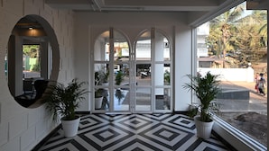 Un hall d’entrée avec un sol à motifs géométriques, des murs blancs et deux plantes en pot.