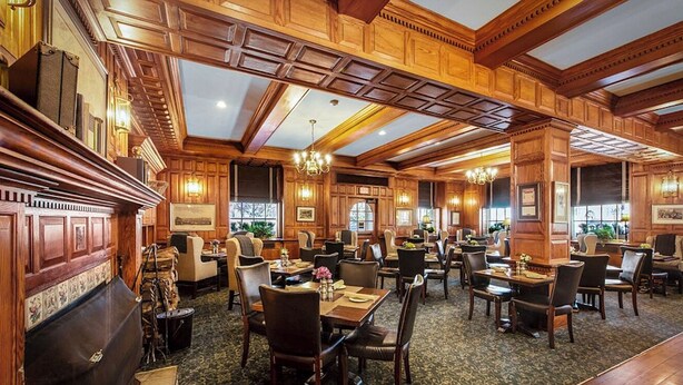 Een ruime hotel eetzaal met houten lambrisering, meerdere tafels en stoelen.
