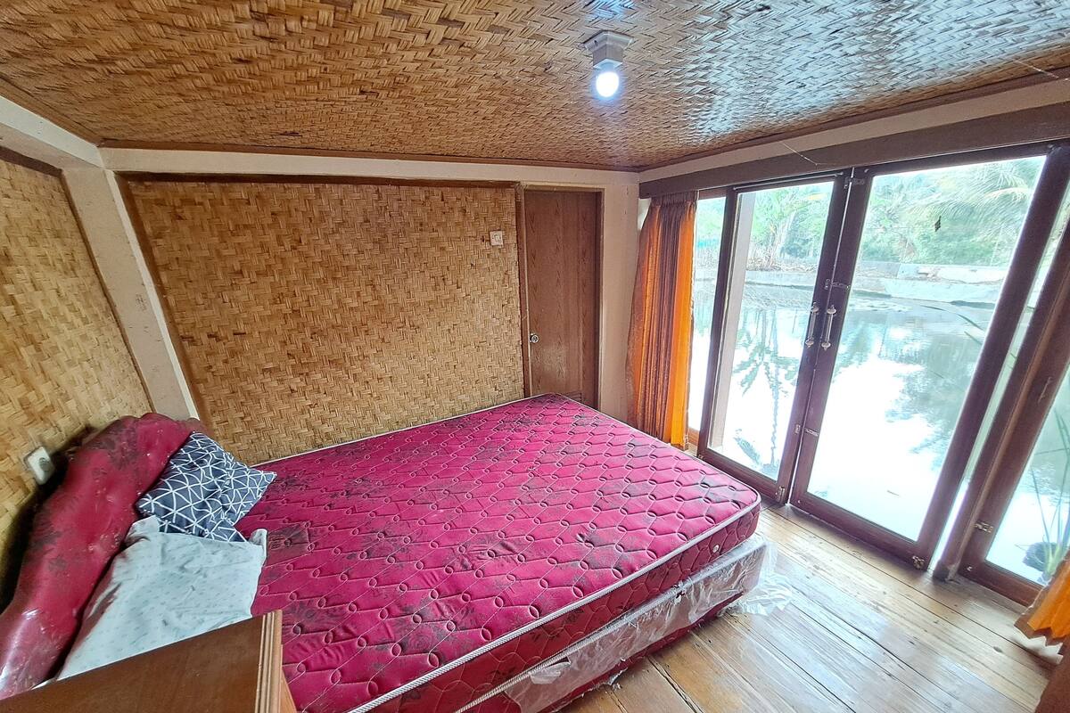 A room with a red mattress, wooden floor, and a woven ceiling.