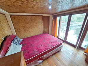 Una habitación con un colchón rojo, suelo de madera y techo tejido.
