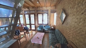 A room with a wooden ceiling, a patterned sofa, a checkered table, and a large window with a view of the outside. - OYO 93656 Villa Cassanova Syariah (Garut)
