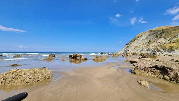 Ein Strand mit großen Felsen und blauem Himmel.