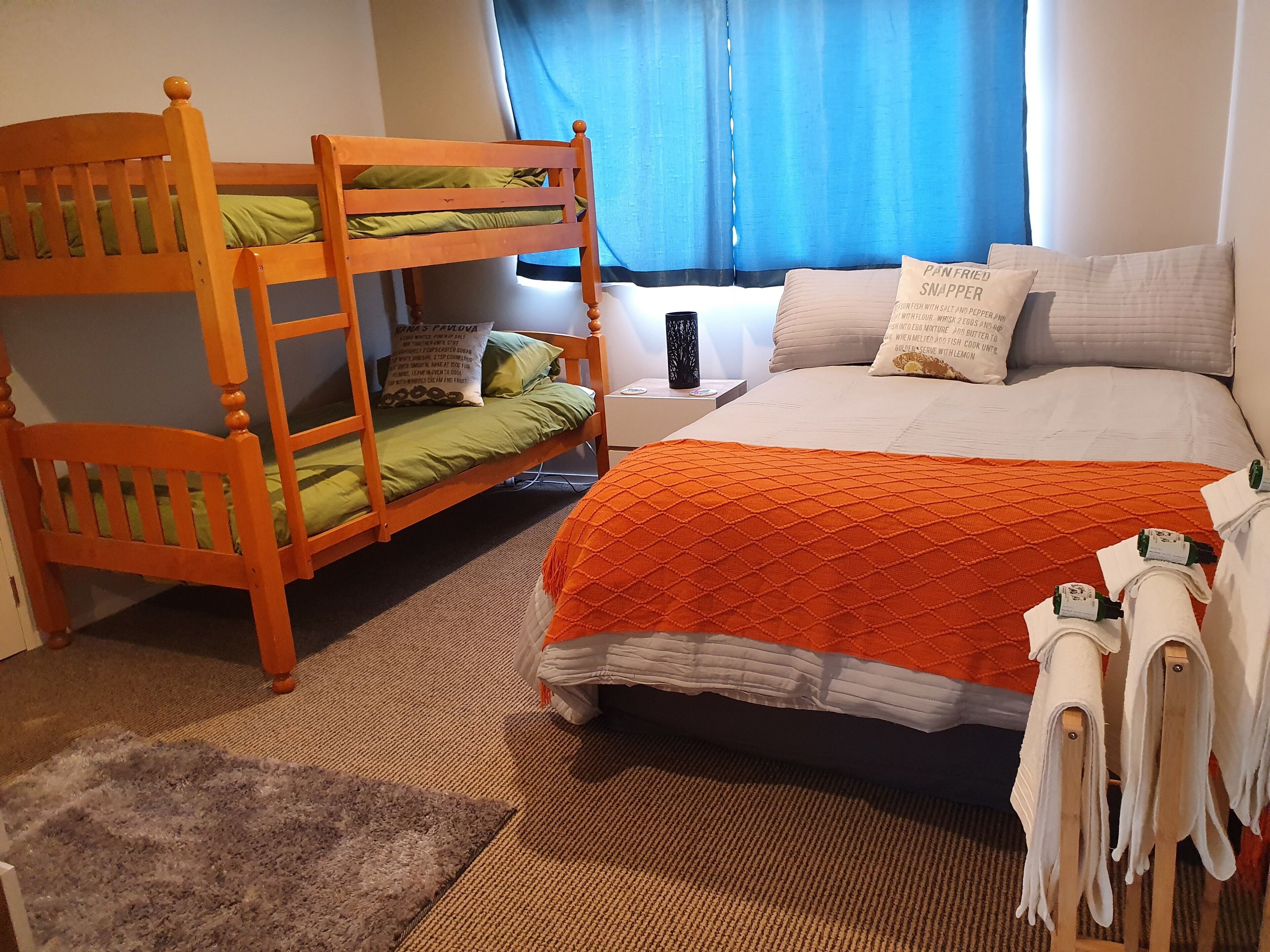 A room with a bunk bed, a single bed, a nightstand, and a window with curtains.