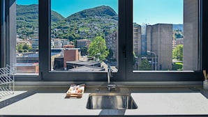 A kitchen with a large window, a stainless steel sink, and a view of a hillside town. - Central Plaza Apartment 3 in Lugano (Lugano)