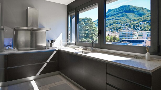 A modern kitchen with a large window, stainless steel appliances, and a view of a mountain. - Central Plaza Apartment 3 in Lugano (Lugano)