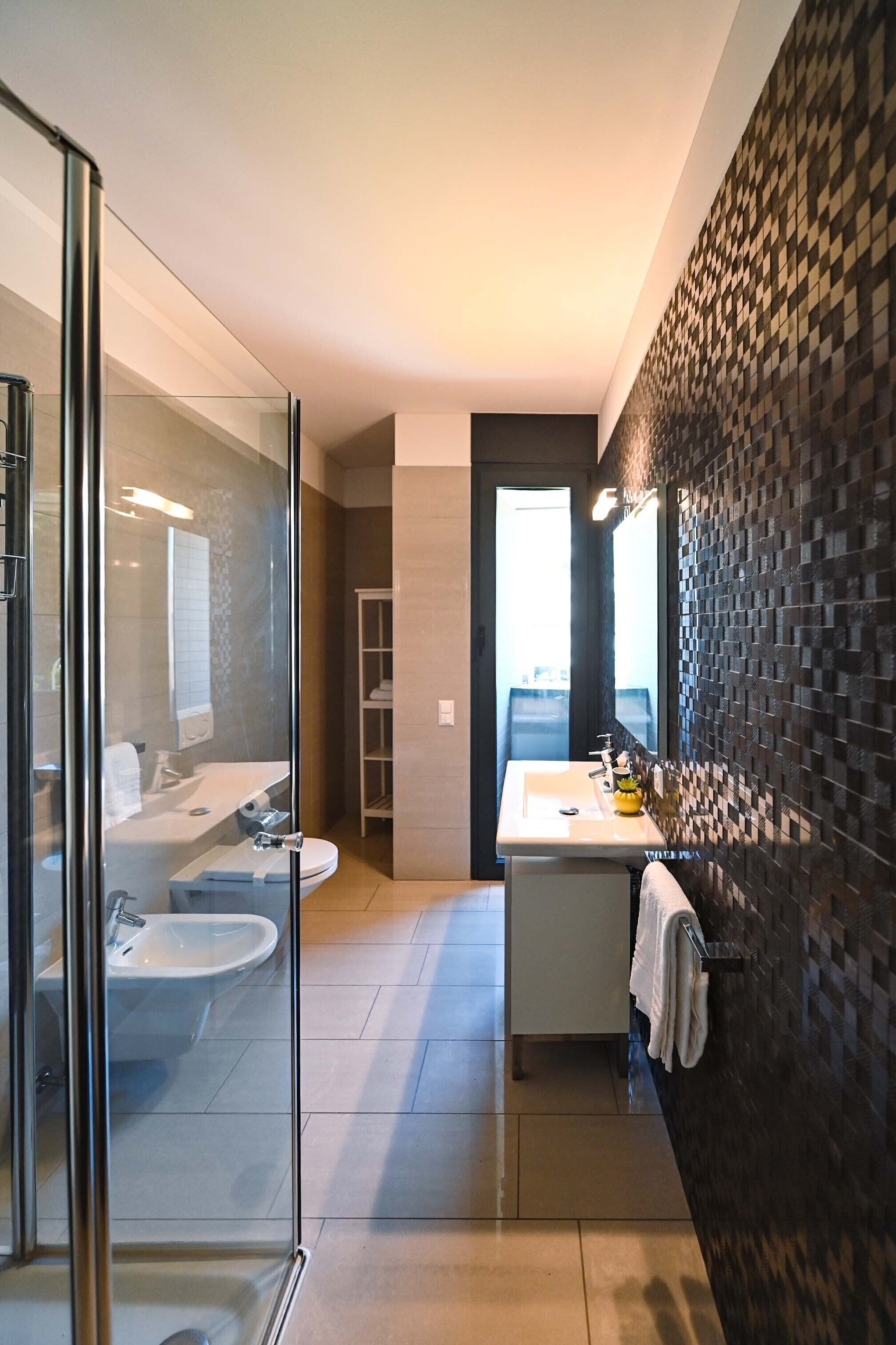 A modern bathroom with a glass shower enclosure, a white sink, and a dark patterned wall.