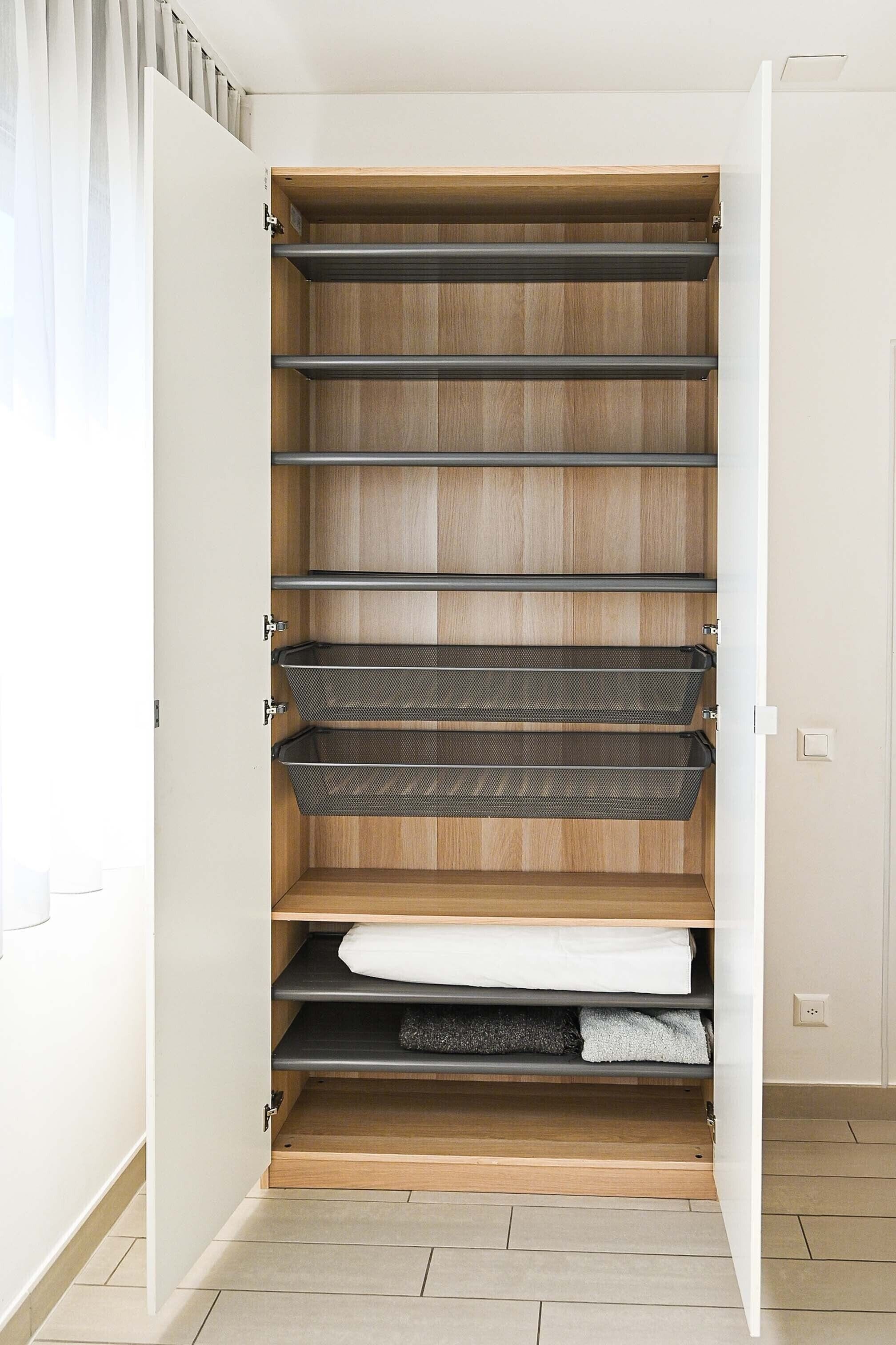A walk-in closet with multiple shelves and hanging space, wooden flooring, and a white door.