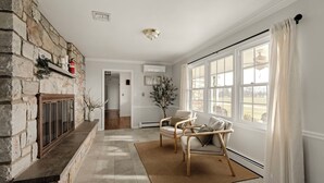 Un salon doté d’une cheminée en pierre, d’une grande fenêtre avec des rideaux et d’un plancher en bois.