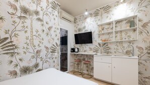A bedroom with a bed, a desk with a sink, a TV, and a shelf with decorative items. - Cozy Love Nest Steps from Colosseum (Roma)