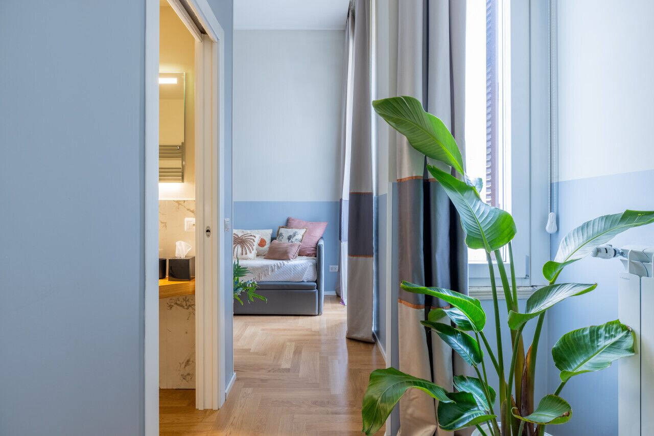 A hallway leading to a bedroom with a bed, a bedside table, and a potted plant.
