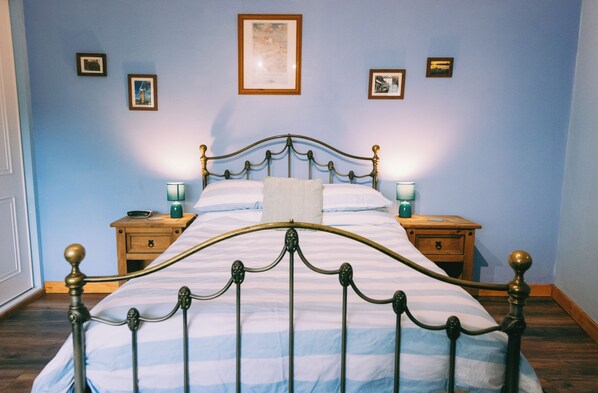 A bed with a metal frame and a striped bedspread, two bedside tables with lamps, and framed pictures on the wall. - Cozy Scarning Apartment for one (Dereham)