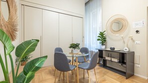 A modern dining area with a round glass table, grey upholstered chairs, and a black console table with decorative items. - Tiberia Room - Suites Romae Rex (Roma)